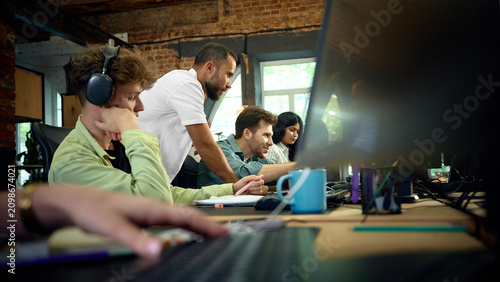 Employees working together at computer screens in modern open plan office. Concept of digital teamwork, software collaboration and coordinated office productivity.