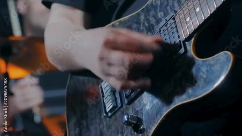 Close up rock guitarist strumming worn black electric guitar under stage lights