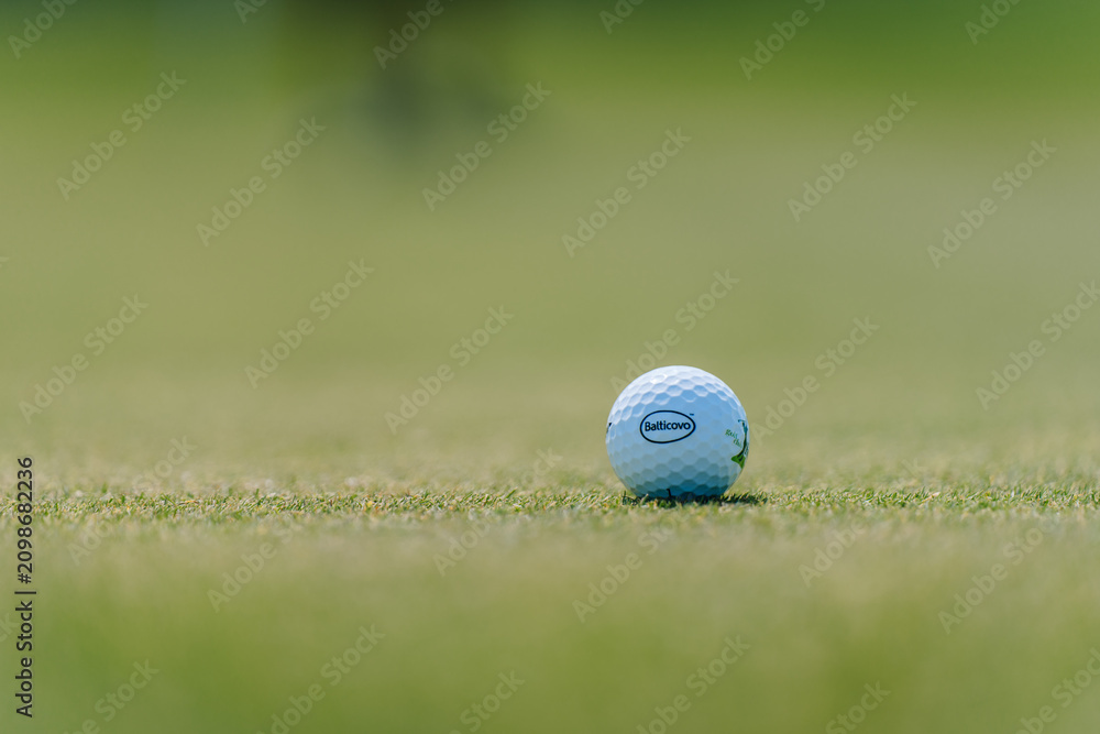 Fototapeta premium Close-up of a golf ball resting on green grass with blurred background, showcasing the brand logo and surface texture