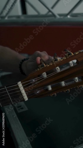 Musician adjusting nylon string guitar tuning pegs before studio performance session
