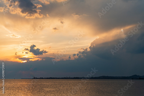 Photos A serene and minimalist view of Lake Constance (Bodensee) at sunset, seen from the Austrian shore in Bregenz, Vorarlberg, featuring warm golden reflections on calm water beneath a soft, dramatic sky