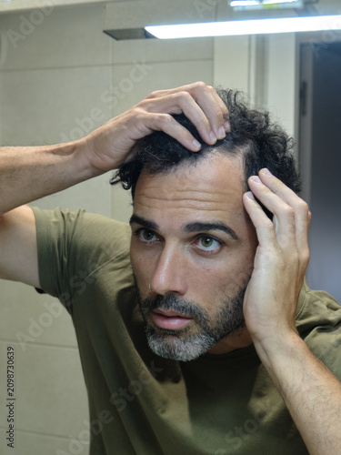 Man checking hair loss in bathroom mirror