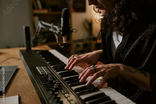 Bild auf Leinwand Close up of young adult musician playing keyboard at home studio, recording original rock music with microphone