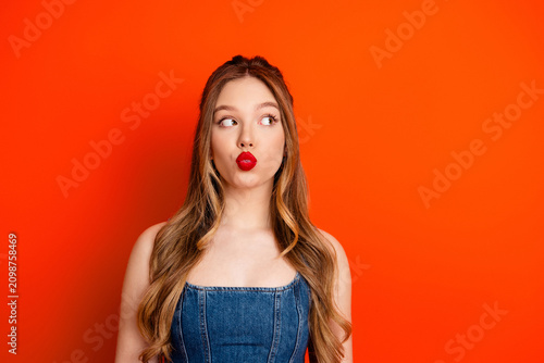 Foto Young woman making a playful kissy face looking sideways against a bright red ba