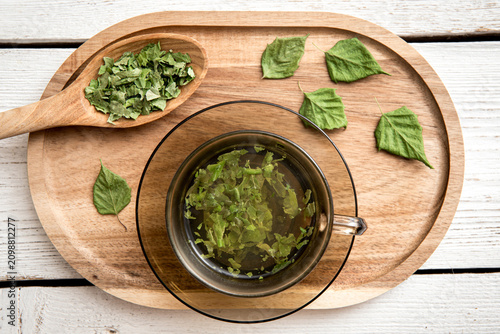 Dried Birch tree leaf powder tea drink in glass cup, Betula powder on a wood spoon on white wood board background.