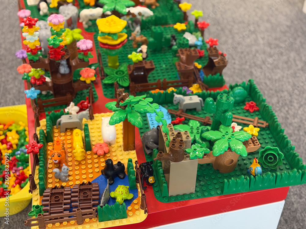 Fototapeta premium Colorful lego-style toy jungle scene with animals, trees, flowers, and small buildings on a play table