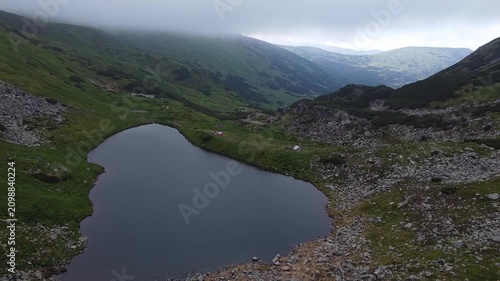 Drone flight over high mountain lake surrounded by green slopes
