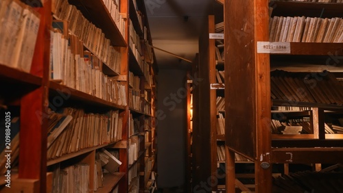 Принти на полотні Old archive folders with radio reel recordings stand on wooden shelves in warm light