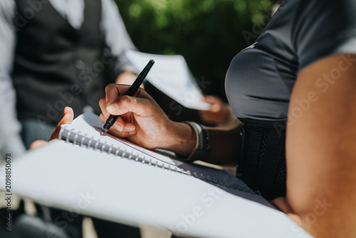 Фотография Person writing with a pen in a spiral notebook during a group meeting