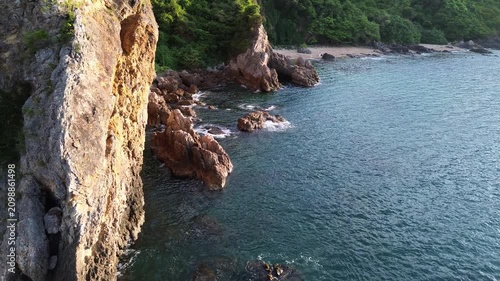Arial view of rocky coastline, trees and sandy beach by the sea