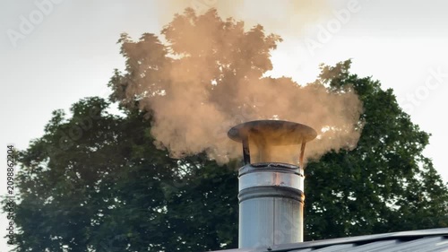 Smoke rises from a metal chimney on a red wooden roof against a cloudy sky. heating, winter home, cozy rural life.