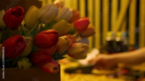 Fresh bouquet of red and white tulips displayed at a flower shop while customer pays by card in the background creating a romantic shopping atmosphere before a date or special occasion