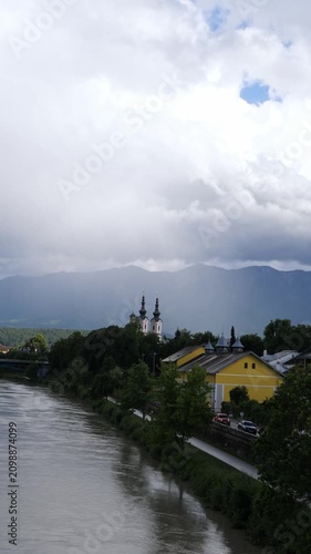 Swollen muddy river flows past an alpine village under heavy rain clouds