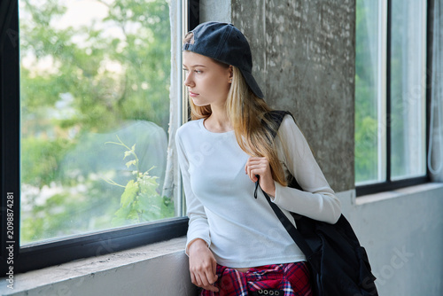 Pensive 16-year-old teenage girl with backpack looking out window