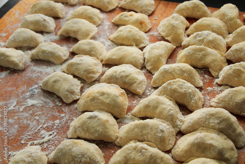 Принти на полотні Raw handmade dumplings dusted with white flour on a rustic wooden board, arrange