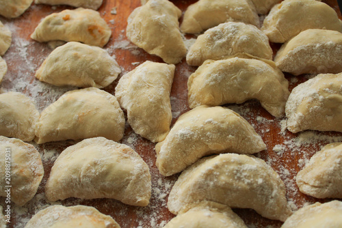 Принти на полотні Freshly made raw dumplings dusted with white flour on a rustic wooden board, showing traditional culinary process with a close-up perspective