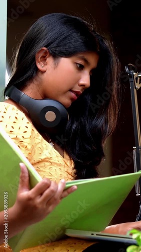 Indian Asian teenage girl studying online at home using a laptop computer while sitting by a bright, airy window in a cozy lavish home, focused on education, exam preparation, learning with dedication