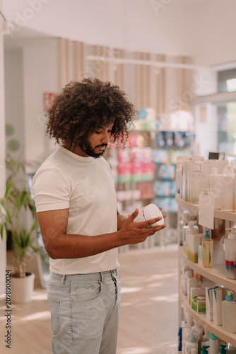 Male customer standing and reading label of product while shopping in pharmacy