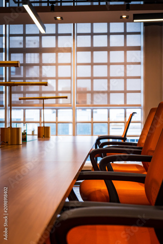 Modern conference room with wooden table, orange chairs, and brass table lamps, empty boardroom interior