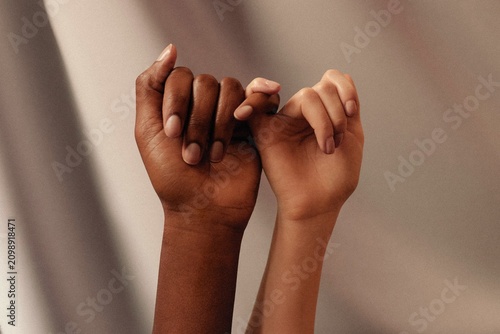Two diverse hands making pinky promise gesture against beige fabric background