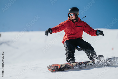 Fotografie A snowboarder in a red jacket and black helmet carves across a snowy slope