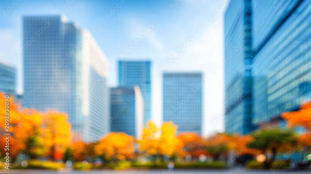 Fototapeta premium ビルと紅葉の木々に囲まれた青空広がる秋のぼかし都市風景
