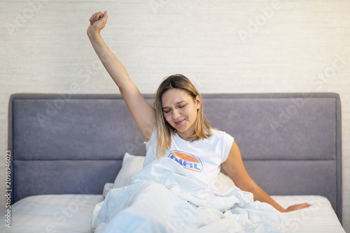 Fotografía Woman yawning and stretching with arms raised in bed after waking up