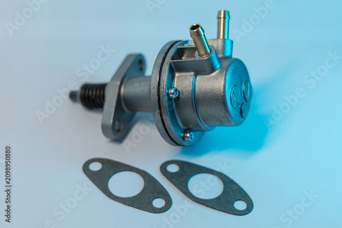 mechanical fuel pump with metal fittings and a spring-loaded lever, photographed with matching rubber gaskets under white and blue lighting on a studio background