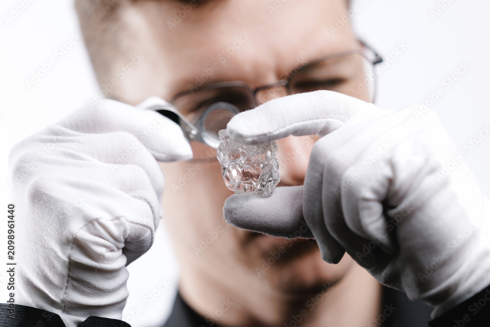 Fototapeta premium Male jeweler inspecting raw diamond with magnifier and gloves