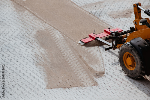 Worker sweeping sand into paver joints during patio installation