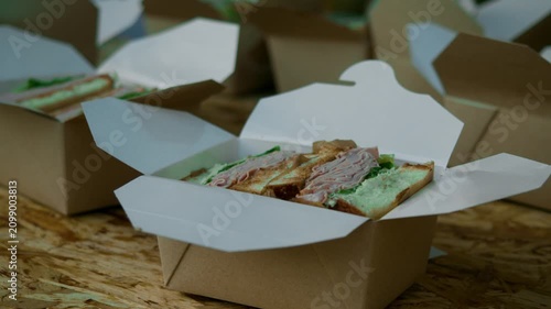 Fresh sandwich waits in takeaway box at street food stall. Packed fast food is ready for customer during evening outdoor food festival.