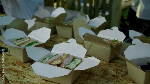 Takeaway sandwich boxes are arranged on counter at street food stand. Catering service prepares fast food orders for outdoor food festival.