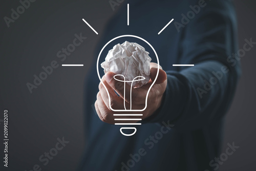 Obraz na plátně Hand holding crumpled paper with light bulb icon representing creativity, innovation, problem solving, brainstorming, startup ideas, business inspiration, and creative thinking concepts