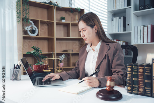 Legal Consultation: Two professionals sit at a desk, carefully reviewing and signing legal documents. In the background a scale of justice rests, and a gavel sits nearby.	
