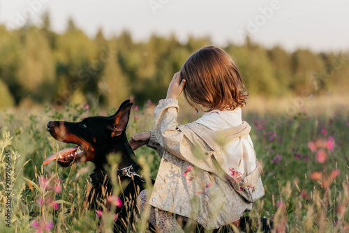 Obraz na plátně A Doberman dog and a little girl, relaxing in a summer field