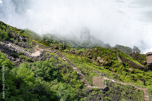 Wooden stairs on mossy rocky cliffs enveloped in thick mist at Niagara Falls.