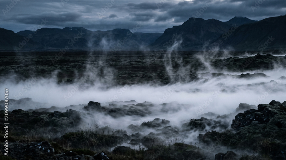 Obraz premium Mist rising from dark volcanic landscape.