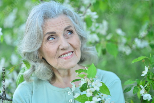 фотографія senior woman smiling and looking up outdoors in spring setting with blossoming trees, happy and serene mood, close-up slightly above eye level, light green and white cloth, nature and bloss