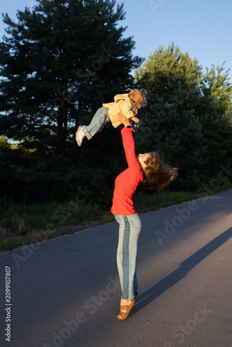 A young mother lifts her little one high in her arms, bringing her joy and delight. happy childhood, the joy of a walk. The sunlight illuminates them. atmosphere of positivity and joy of motherhood