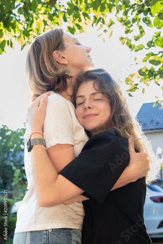 tender portrait of woman (around 40 years old) and her teenage daughter, embracing affectionately in glow of backlight. Generational closeness. Family support and love. Mother's Day. Daughter's Day