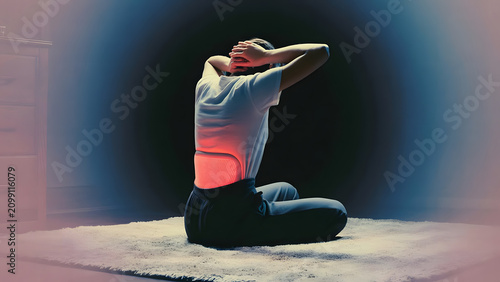 Person sitting on carpet clutching head, glowing red light on lower back representing spine pain or heat therapy, backache and wellness concept on dark background
