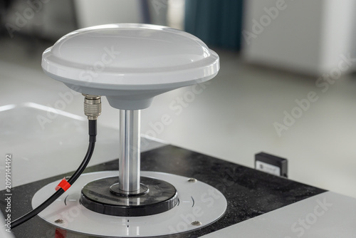 Canvastavla White dome GPS antenna mounted on a metal pedestal with a coaxial cable connection, photographed in a clean laboratory setting
