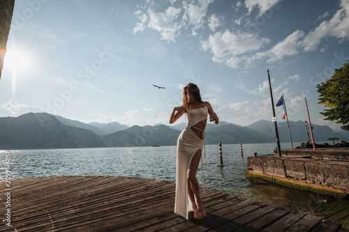 Fotografie Model poses on a wooden pier by Lake Garda in Italy during daylight, with mounta