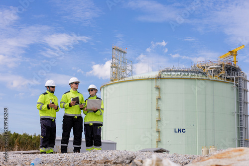 Team of engineers working together on the construction site of a liquefied natural gas facility with bright blue skies above