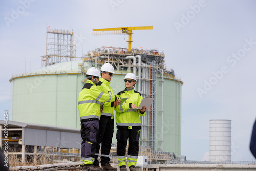 Team of engineers wearing safety gear working together on a construction site with an industrial building in the background