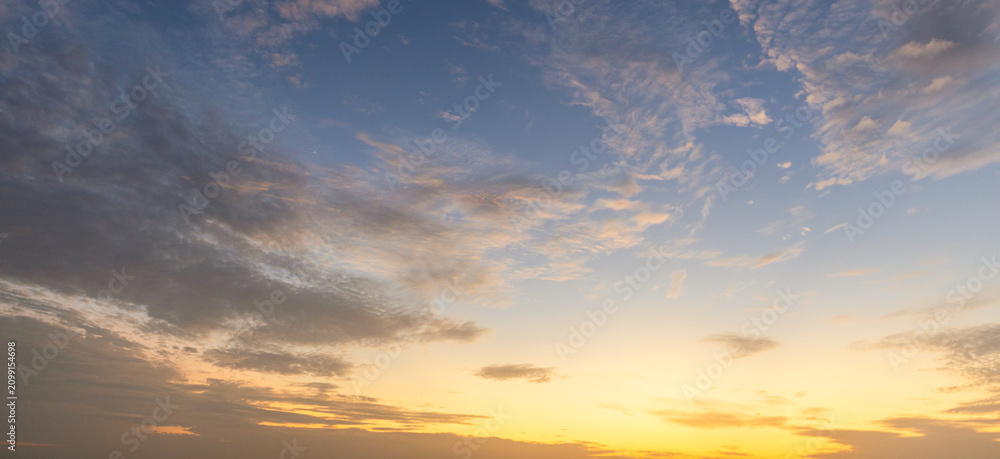 Naklejka premium Dramatic golden hour sky with soft clouds at sunset,A beautiful and serene view of a golden hour sky, featuring soft, wispy clouds illuminated by the warm, gentle light of the setting sun, creating.