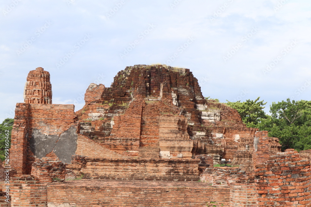 Fototapeta premium Ancient Ruins of Ayutthaya: Weathered brick structures and crumbling stone edifices stand testament to the passage of time, evoking a sense of historical grandeur and mystery amidst lush greenery.