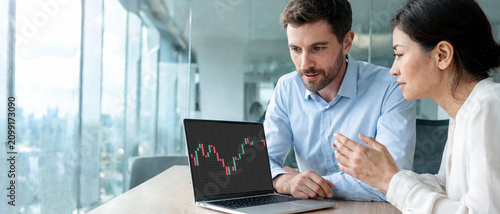 Socios comerciales analizando un gráfico técnico de trading en una laptop dentro de una moderna oficina corporativa. Concepto de trabajo en equipo, inversiones y finanzas corporativas.