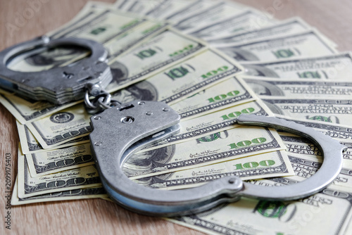 Bild auf Leinwand Metal handcuffs resting on spread US dollar banknotes on wooden surface, symboli