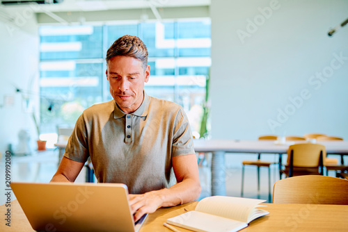 Bild auf Leinwand Professional man concentrating on his computer, sitting at a desk in a bright, c